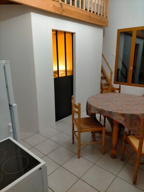 Un coin repas avec une table et des chaises, une fenêtre donnant sur un paysage agréable, un escalier et un réfrigérateur.