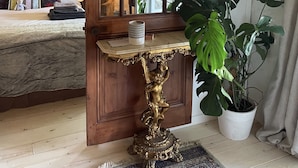 Una habitación con una cama, una puerta de madera, una mesa con una planta y un candelabro.