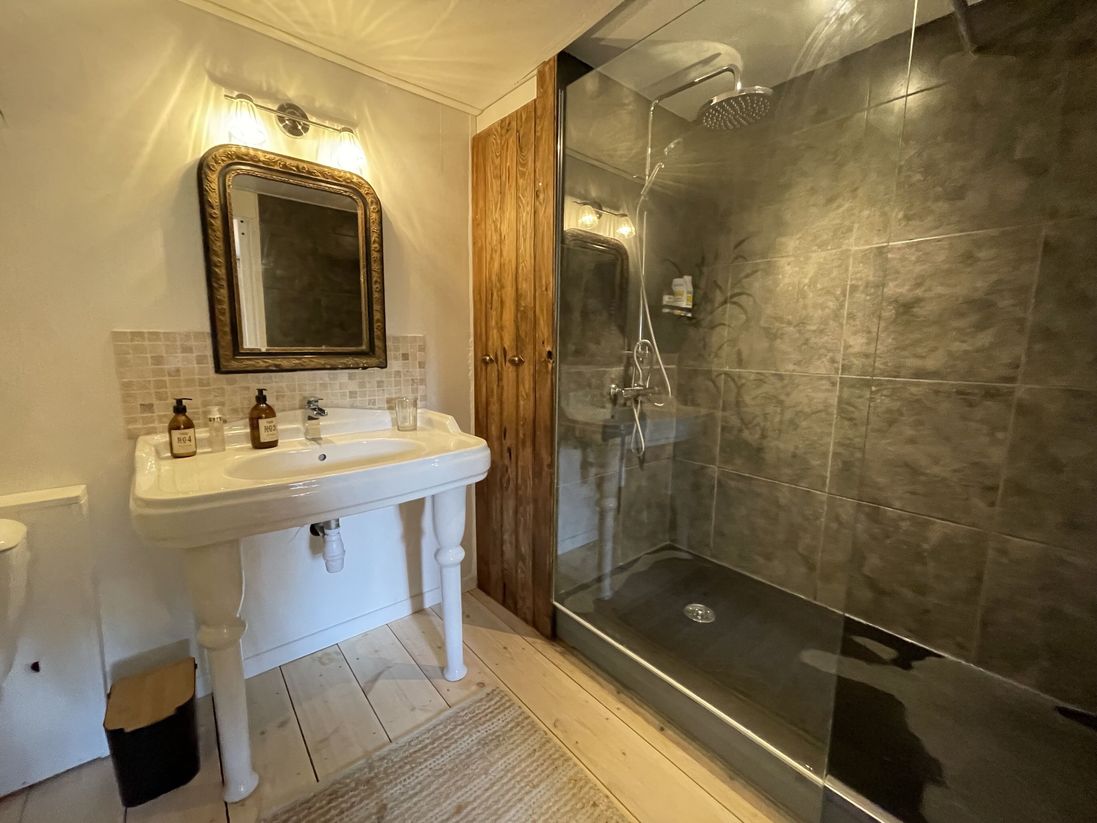 Une salle de bain avec un lavabo blanc, un miroir et une porte en bois.