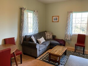 Un salon avec un canapé, une table basse et des fauteuils. Il y a deux fenêtres avec des rideaux à motifs.