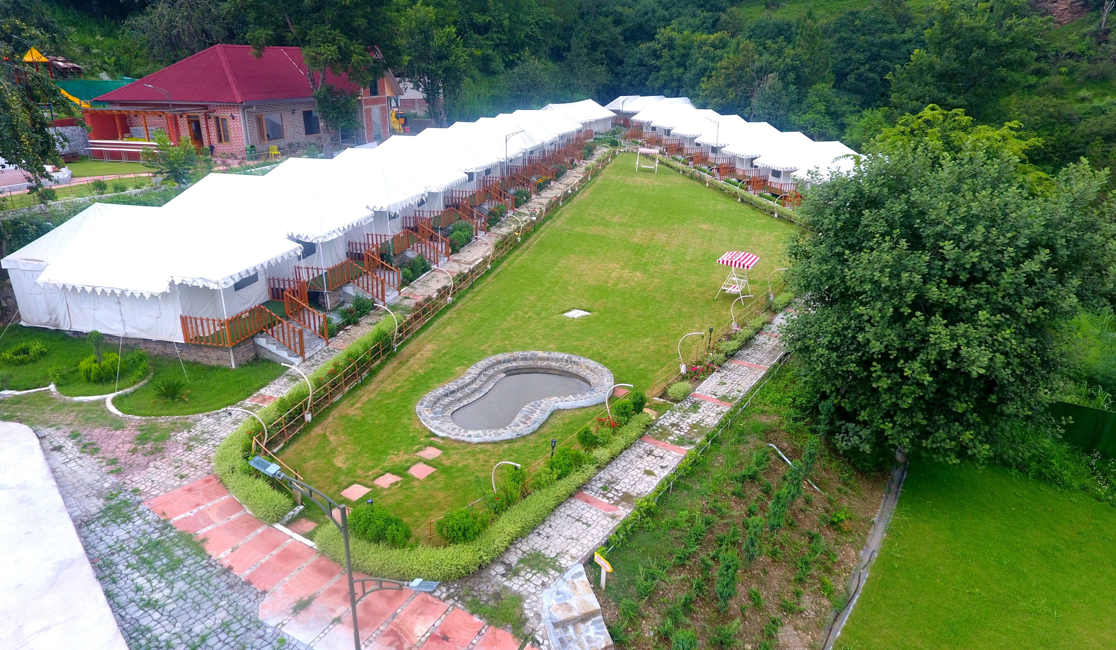 A courtyard with white tents, a stone pool, and a red-roofed building.