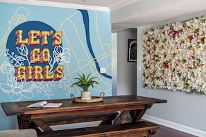 Un mur orné de l’inscription « ALLONS-Y, LES FILLES », une décoration murale florale et un banc en bois avec un pot de plante.