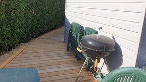 A wooden deck with a barbecue grill, green chairs, and a blue table. - BEAUTIFUL BRAND-NEW STUDIO APARTMENT (Le teich)