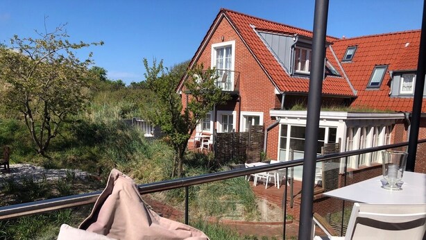 Een balkon met een tafel en stoelen, met uitzicht op een tuin en een gebouw met rode dakpannen.