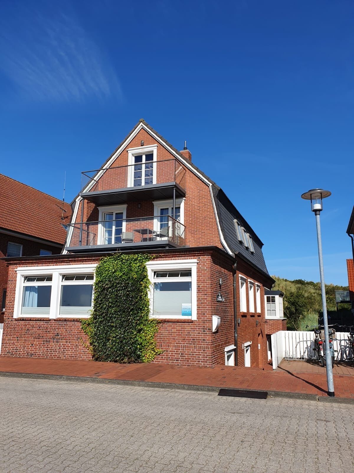 Ein zweistöckiges Backsteinhaus mit Balkon, kleinem Garten und einer Straßenlaterne.