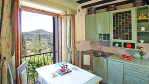 Une cuisine donnant sur la campagne, une table à manger avec une théière rouge et des meubles de couleur verte.