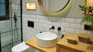 Un bany modern amb dutxa envidriada, un lavabo blanc amb taulell de fusta i un mirall amb marc de fusta.