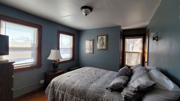 A bedroom with a bed, two windows, a lamp, and framed pictures on the wall. - Cute & cozy 1 bedroom apartment - sleeps 4 (Negaunee)