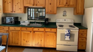 Una cocina con armarios de madera, microondas, pileta, estufa y refrigerador.