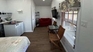 A compact kitchen with a sink, stove, and refrigerator, a dining area with a table and chairs, and a red sofa. - Lakefront Purple Cottage (Northwood)