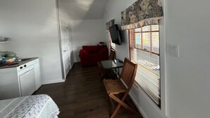 A compact room with a kitchenette, a dining area with a table and chairs, a red sofa, and a television mounted on the wall. - Lakefront Purple Cottage (Northwood)