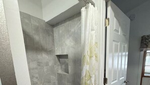 A walk-in shower with grey tiles and a leaf-patterned shower curtain. - Lakefront Purple Cottage (Northwood)