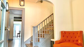 Ein geräumiger Wohnbereich mit Holzboden, einer Treppe und einem leuchtend orangefarbenen Sessel.