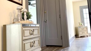 Ein Flur mit Holzboden, einem weißen Schminktisch mit Schubladen, einem gerahmten Gemälde an der Wand und einer geschlossenen Tür.