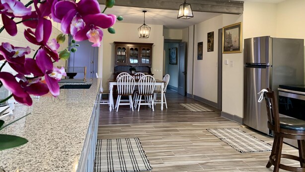 Eine moderne Küche mit einem Edelstahlkühlschrank, Holzschränken und einem Essbereich mit weißen Stühlen und einer Granit Arbeitsplatte.