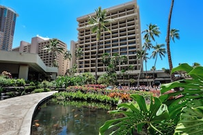 A hotel with a pool, palm trees, and a large building in the background.