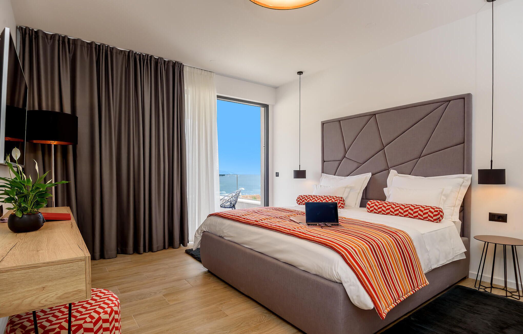 A modern hotel room with a large bed, a desk, a chair, and a view of the sea.