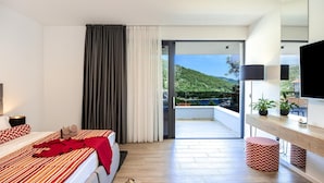 A hotel room with a bed, a bedside table with a lamp, a TV, a window with a view of a hillside, and a balcony with a potted plant. - Luxurious home in Marina with sauna (Marina)