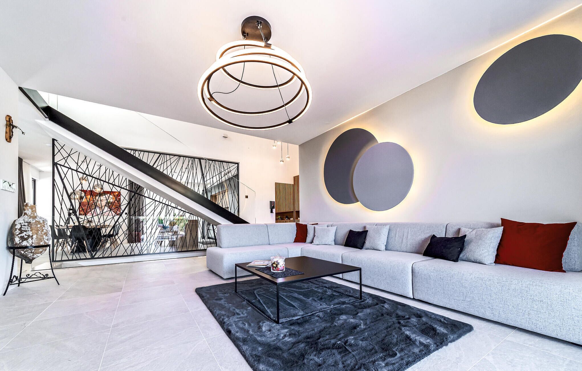 A modern living room with a grey sofa, black coffee table, and a staircase with a geometric railing.
