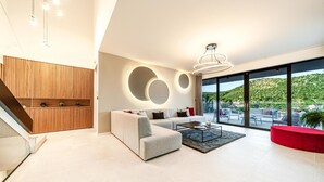 A modern living room with a sofa, coffee table, and a view of a hillside. - Luxurious home in Marina with sauna (Marina)
