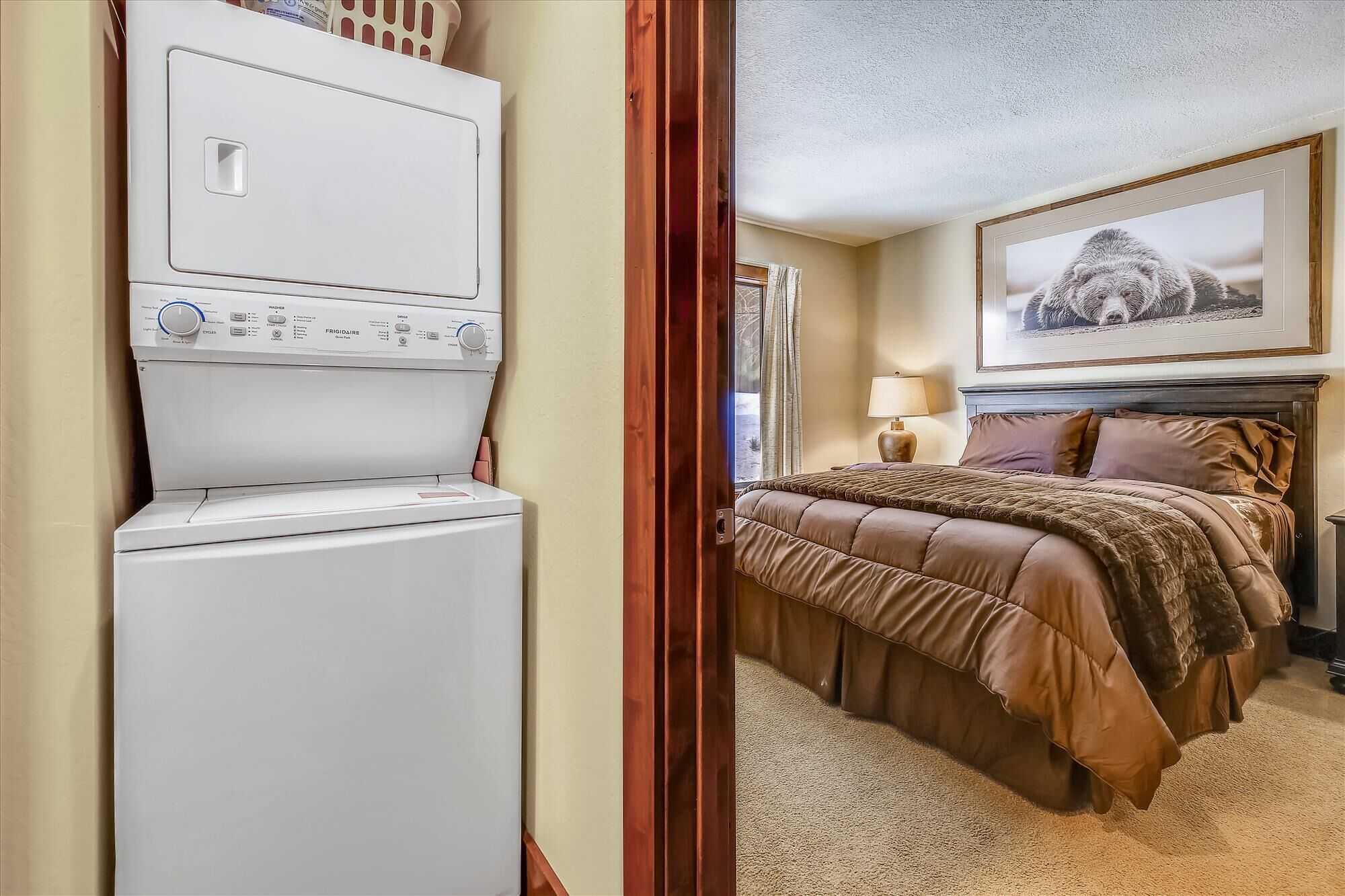 A hotel room with a bed, a lamp, a framed picture on the wall, and a washing machine.