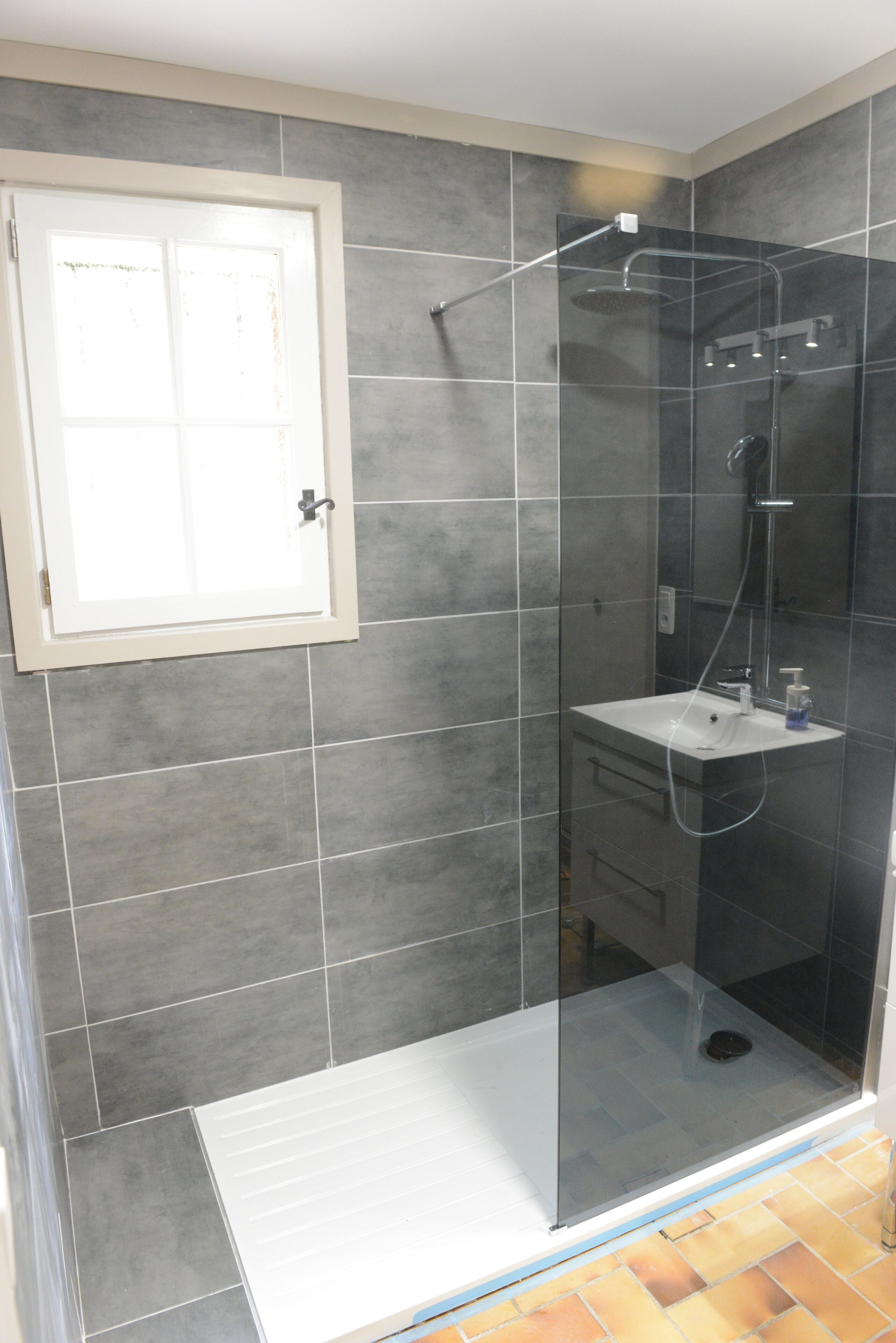 A modern bathroom with a glass-enclosed shower, a white sink, and a tiled floor.