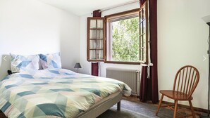 A bedroom with a bed, a window with curtains, a chair, and a radiator. - Villa BELLE-VUE. Fully equipped (Taradeau)