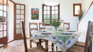 A dining area with a table set for four, surrounded by wooden chairs. There is a window with a view of greenery, a painting on the wall, and a staircase to the right. - Villa BELLE-VUE. Fully equipped (Taradeau)