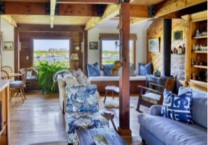 A spacious living area with a wooden ceiling, a sofa set, a dining table, and a view of the outdoors.