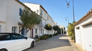 Une rue étroite bordée de bâtiments blancs, une voiture blanche garée sur le côté et un lampadaire.