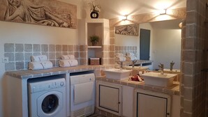 Een moderne badkamer met een betegelde muur, dubbele wastafels, een grote spiegel en een ingebouwde wasmachine.