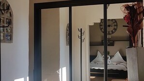 Een kamer met een houten vloer, een bed met wit beddengoed, een klok aan de muur en een groot raam voor natuurlijk licht.