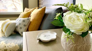 A bedroom with a bed, pillows, a bedside table with a vase of flowers, and a window with blinds.