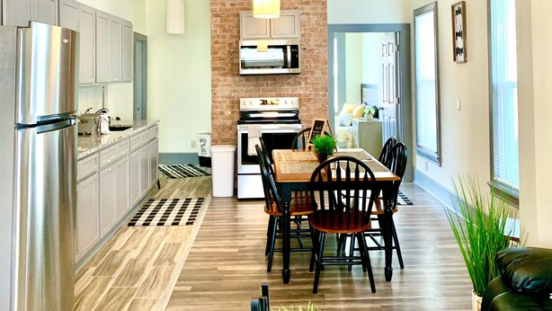A modern kitchen with a brick accent wall, stainless steel appliances, and a dining area with a wooden table and chairs.