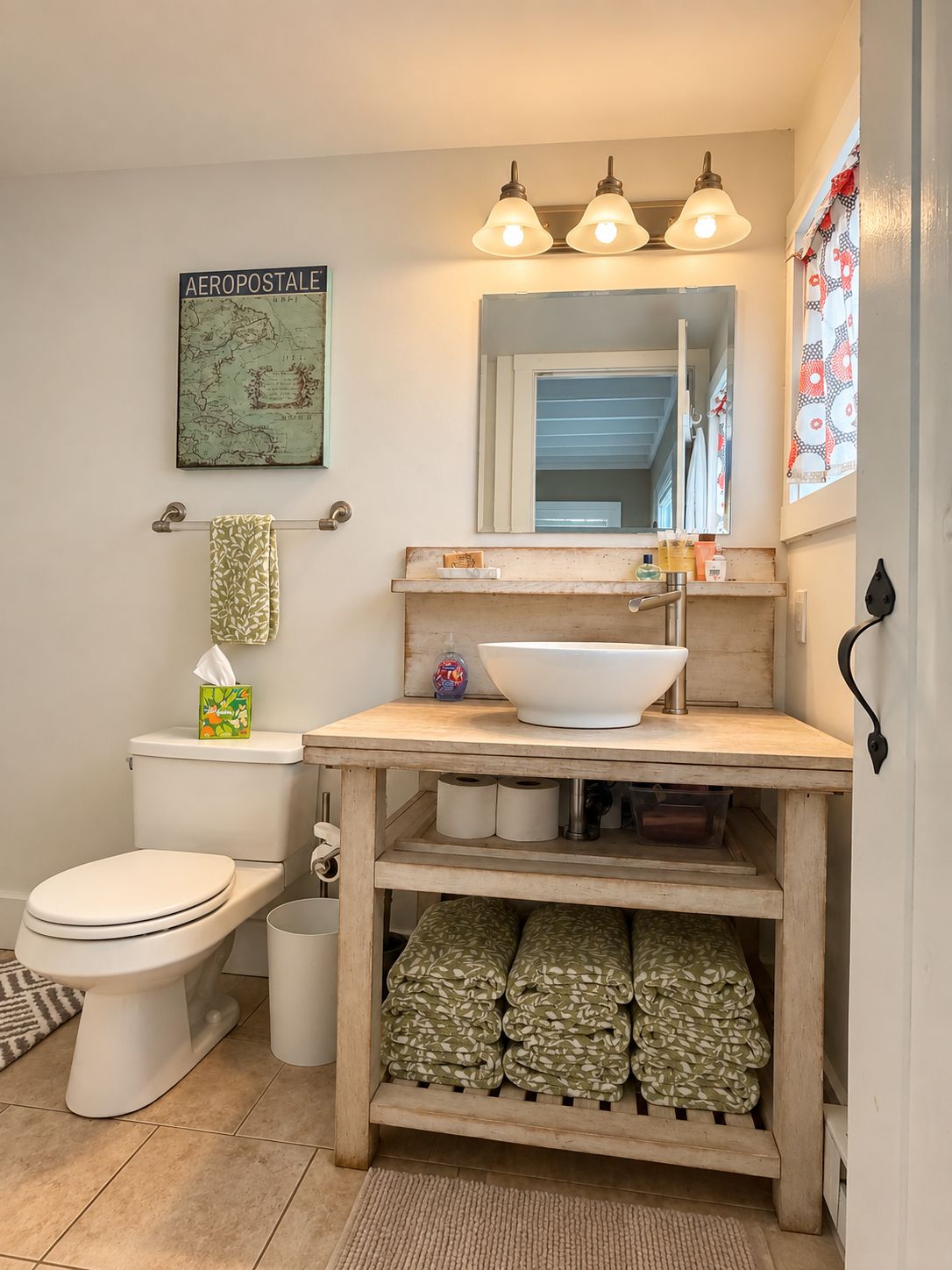 A bathroom with a toilet, a sink with a mirror, a map on the wall, and a shelf with towels.