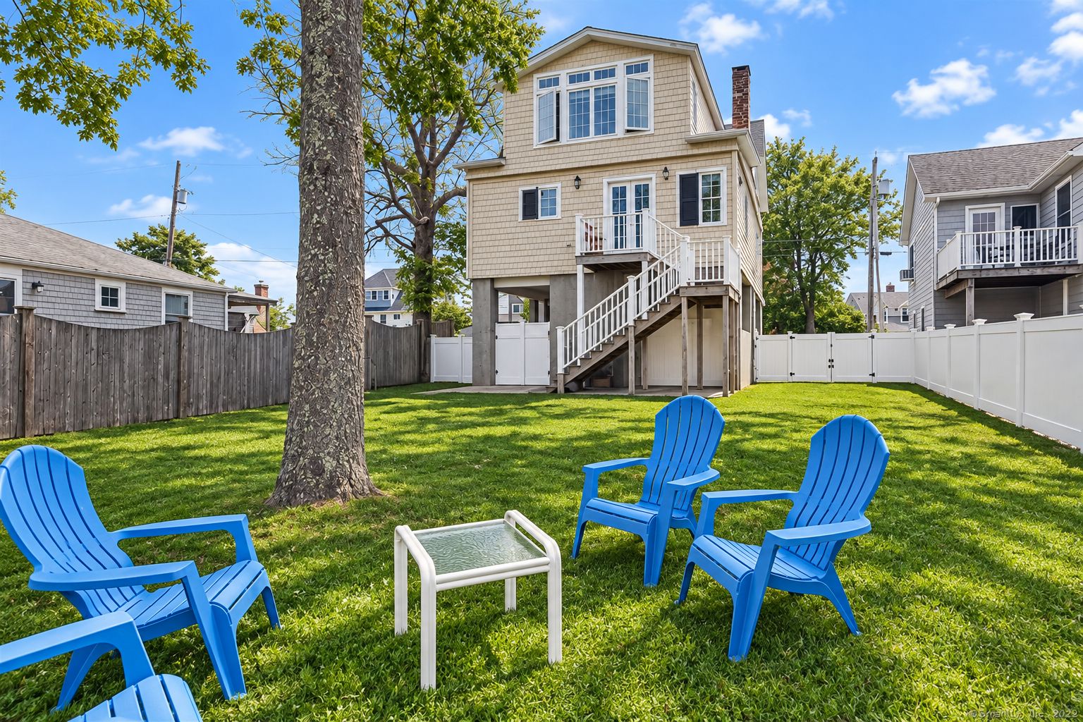 A backyard with a two-story house, a wooden fence, and blue Adirondack chairs.
