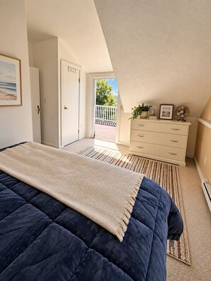 Une chambre à coucher comprenant un lit, une commode, une porte donnant sur un balcon extérieur et un ventilateur de plafond.