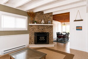 A living room with a stone fireplace, a dining area with a wooden table and chairs, and a view of the outdoors through a window.