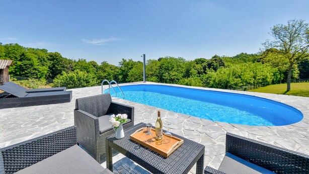 Una piscina con solárium de piedra, rodeada de mobiliario de mimbre y una mesa con una botella y vasos.