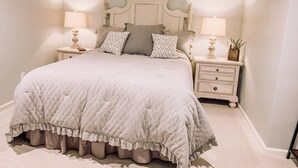 Un dormitorio con una cama grande, dos mesitas de noche con lámparas y un pequeño mueble con una planta.