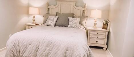 Un dormitorio con una cama grande, dos mesitas de noche con lámparas y un pequeño mueble con una planta.