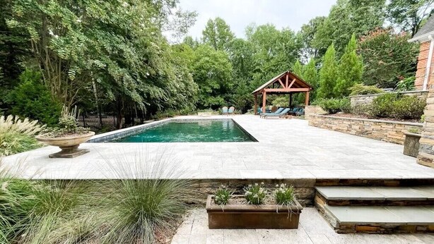 Un patio trasero con piscina, un pergolado de madera y un patio de piedra.