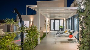 A modern outdoor lounge area with a glass wall, white lounge chairs, and potted plants. - Gorgeous home in Kastelir (Kastelir)