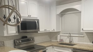 Una cocina con alacenas blancas, encimera de granito, lavavajillas de acero inoxidable y microondas.