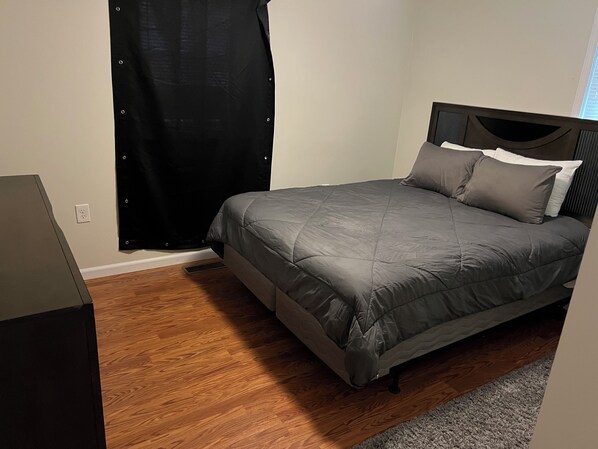 A bedroom with a bed, a window with a black curtain, and a wooden floor. - Quiet Area In The Middle Of Everything. 7 Minutes To Watkins Glen International. (Beaver Dams)