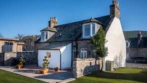 A stone house with a white exterior, a small garden with potted plants, and a paved driveway. - Contemporary Cottage in Ballater Village (Ballater)
