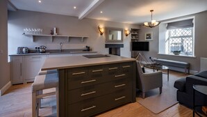A modern kitchen with a central island, built-in appliances, and a dining area with a bench and table. - Contemporary Cottage in Ballater Village (Ballater)