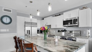 A modern kitchen with white cabinets, stainless steel appliances, a marble island, and wooden chairs. - REMODELED! BeachFront, Bch Service, Pool, wifi, Kitchen, grill (Destin)