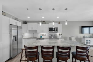 A modern kitchen with white cabinetry, stainless steel appliances, a marble island, and wooden chairs.