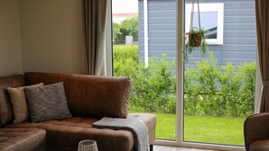 Ett modernt vardagsrum med en brun lädersoffa, ett runt soffbord och utsikt över en grön trädgård genom stora fönster.
